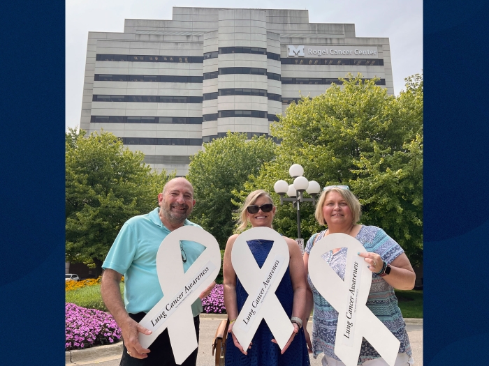 three friends standing outside rogel cancer center building with big white ribbons