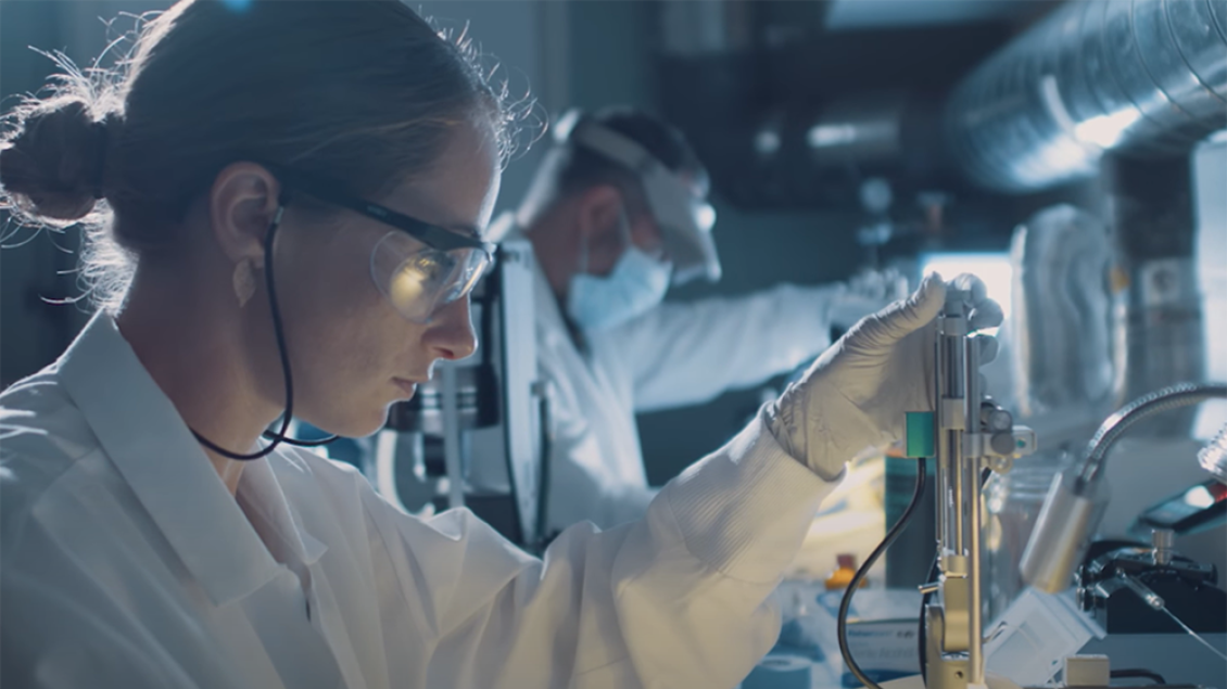 A woman wearing safety glasses works in a laboratory.