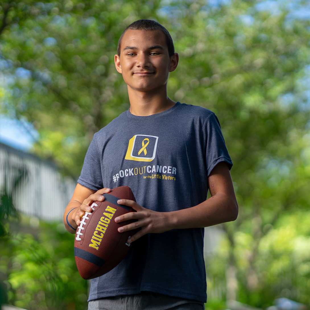 Adolescent boy wearing a block out cancer t-shirt and holding a Michigan footbal 